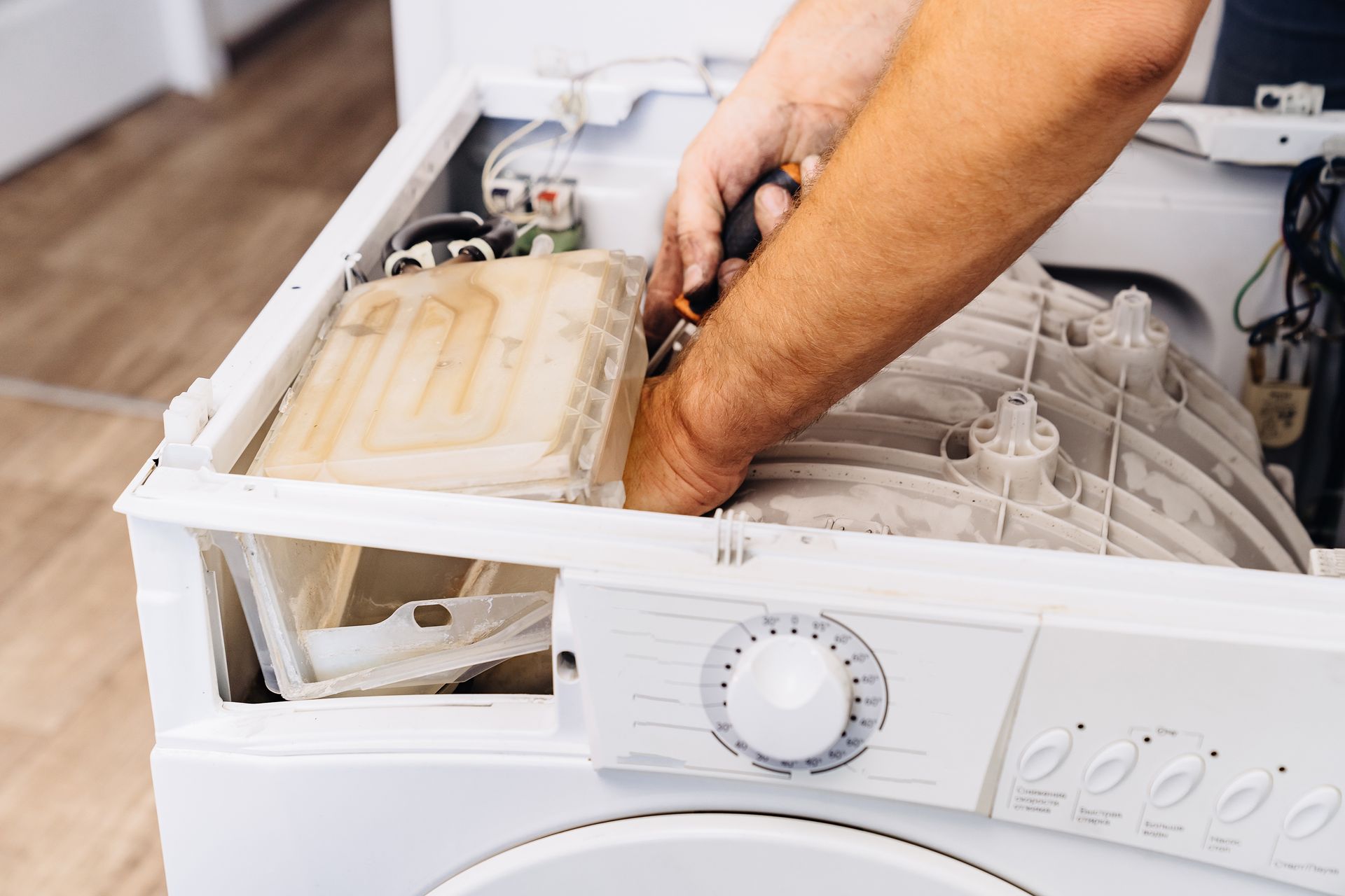 Hands removing a top panel from a white washing machine, exposing internal components.