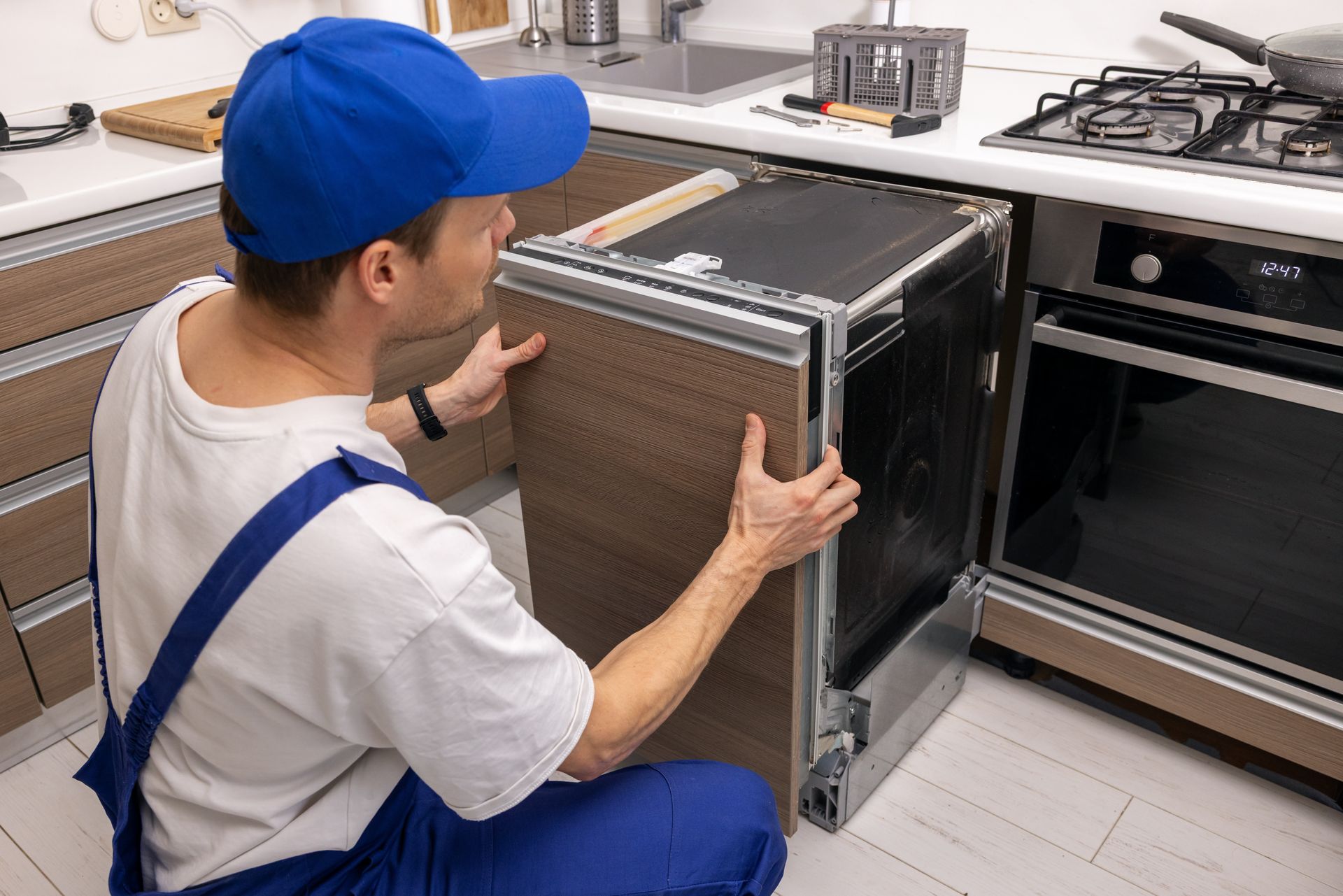 Technician in blue uniform installing an oven in a kitchen with cabinets and countertops