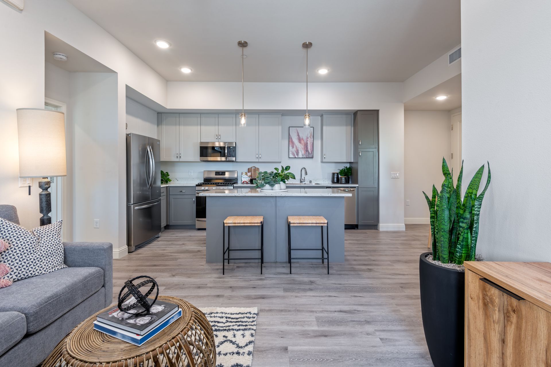 Modern kitchen and living area with gray cabinets, stainless steel appliances, and hardwood floors.