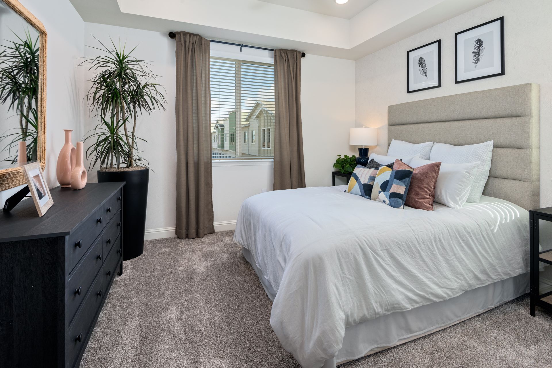 Bedroom with a black dresser, bed, and window with brown curtains. White walls and carpet.