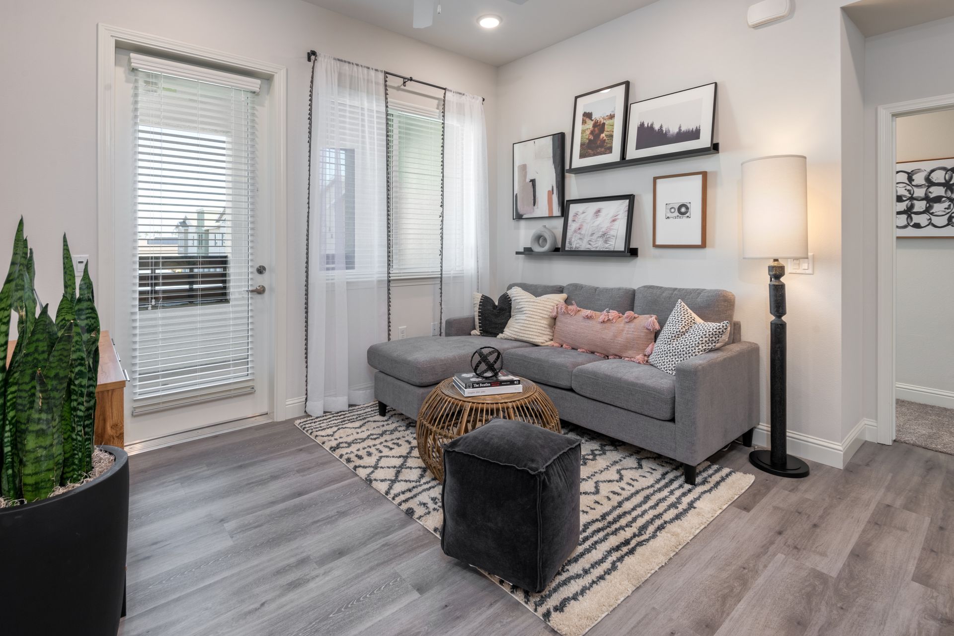 Living room with gray sectional, artwork, rug, and floor lamp. Door to balcony on left.