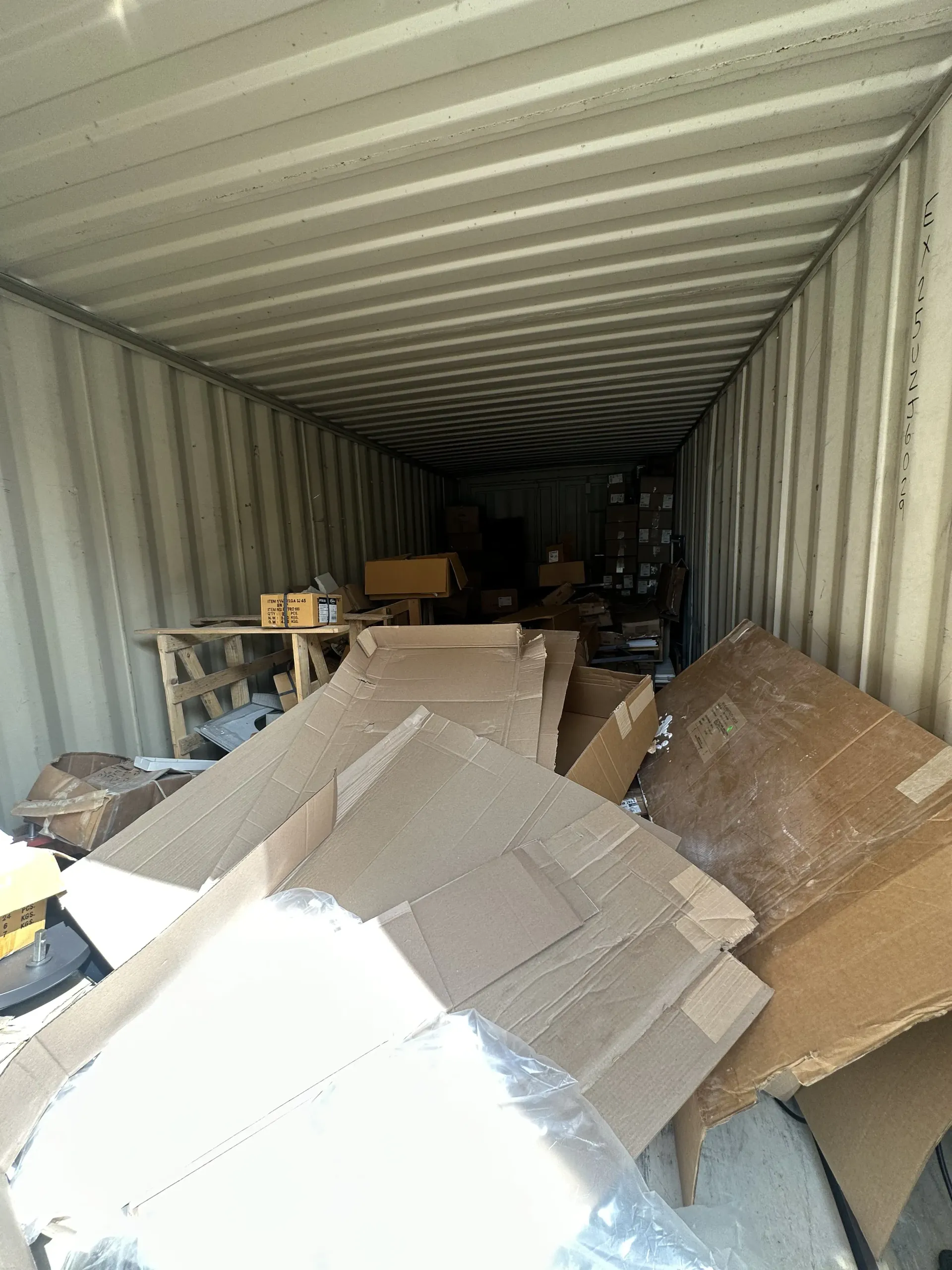 Inside a shipping container, open cardboard boxes and packing materials are scattered along the floor.