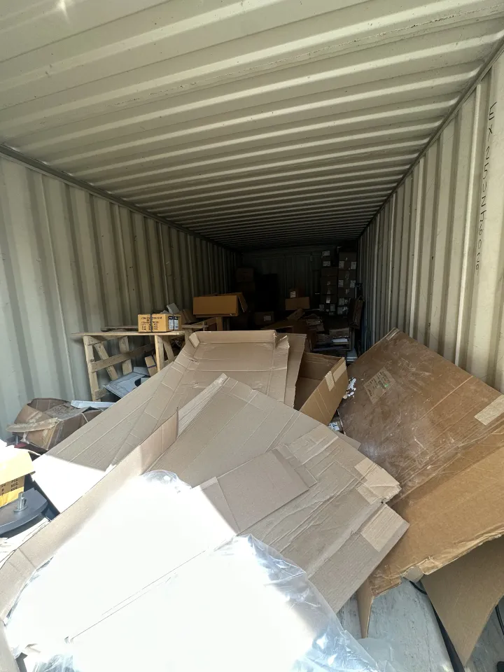 Inside a shipping container, piles of cardboard and packing debris clutter the floor.
