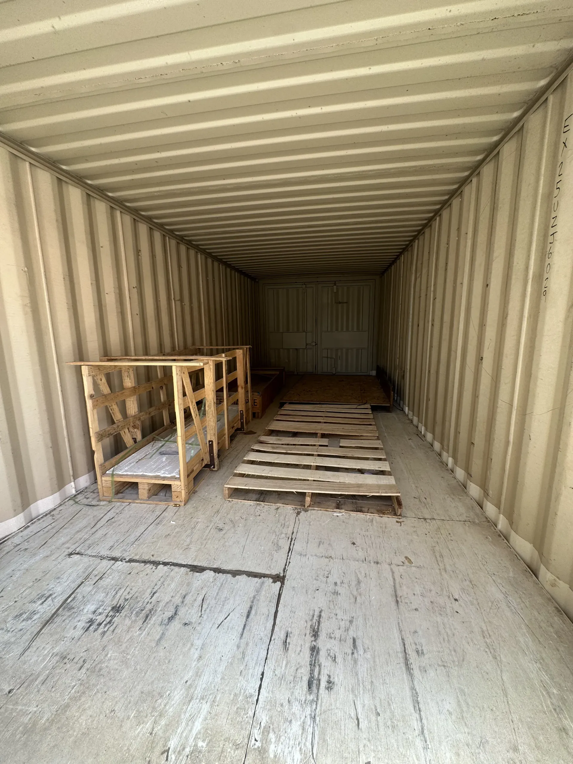Inside an empty shipping container with wooden pallets on the floor and left side.