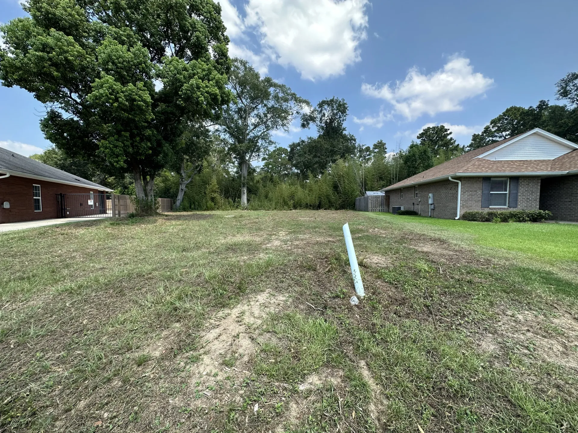 Vacant grassy lot between two brick houses under a partly cloudy sky