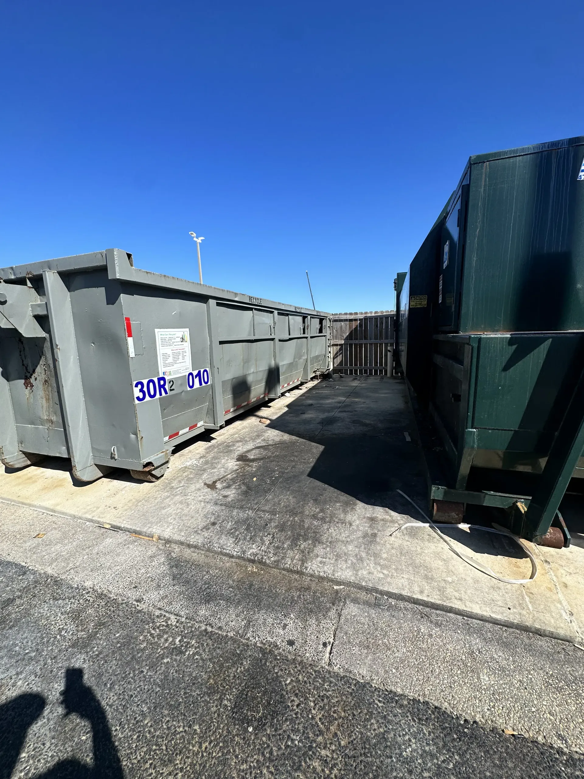 Outdoor alley between large gray dumpsters under a clear blue sky