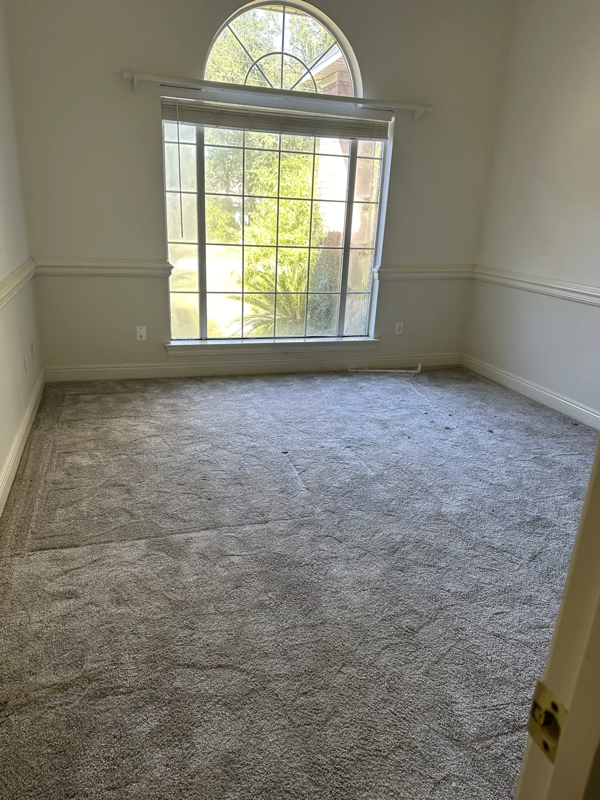Empty carpeted room with large arched window and white walls