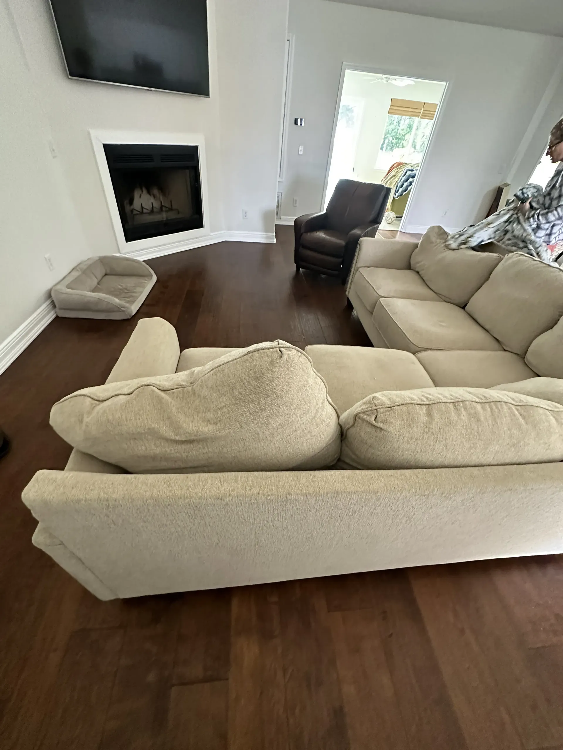 Living room with beige sectional sofa, dark wood floor, fireplace, and chair near a bright doorway