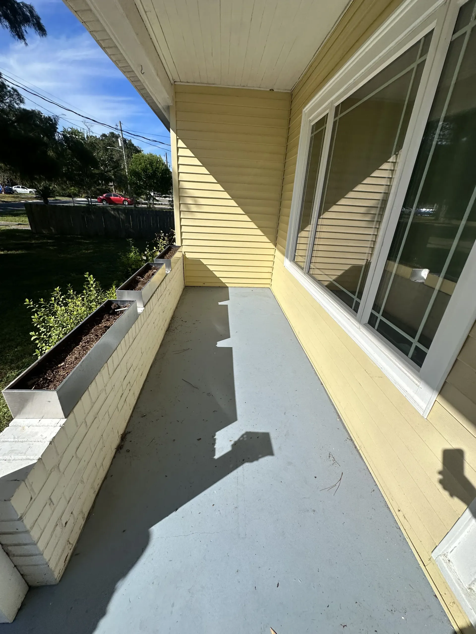 Narrow yellow apartment balcony with white floor, sliding glass door, and railing overlooking trees