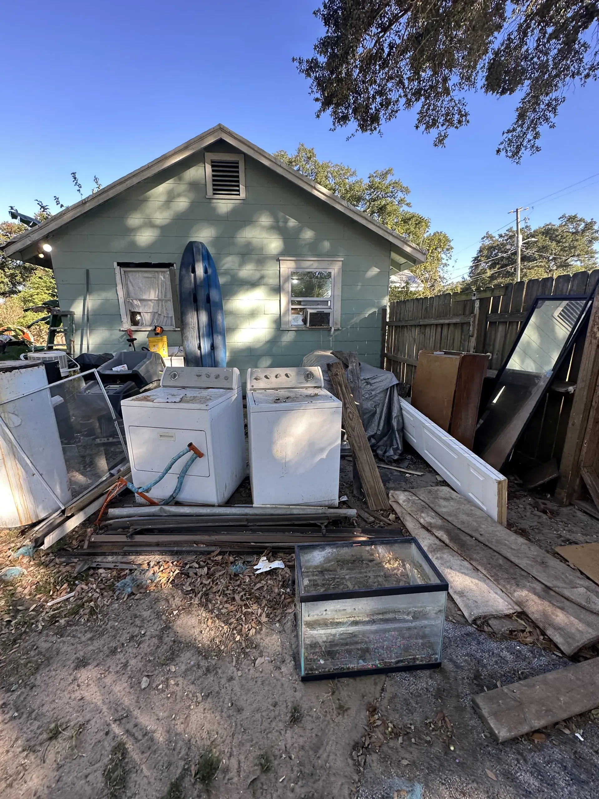 Backyard renovation with stacked cabinets, lumber, and debris in front of a small house