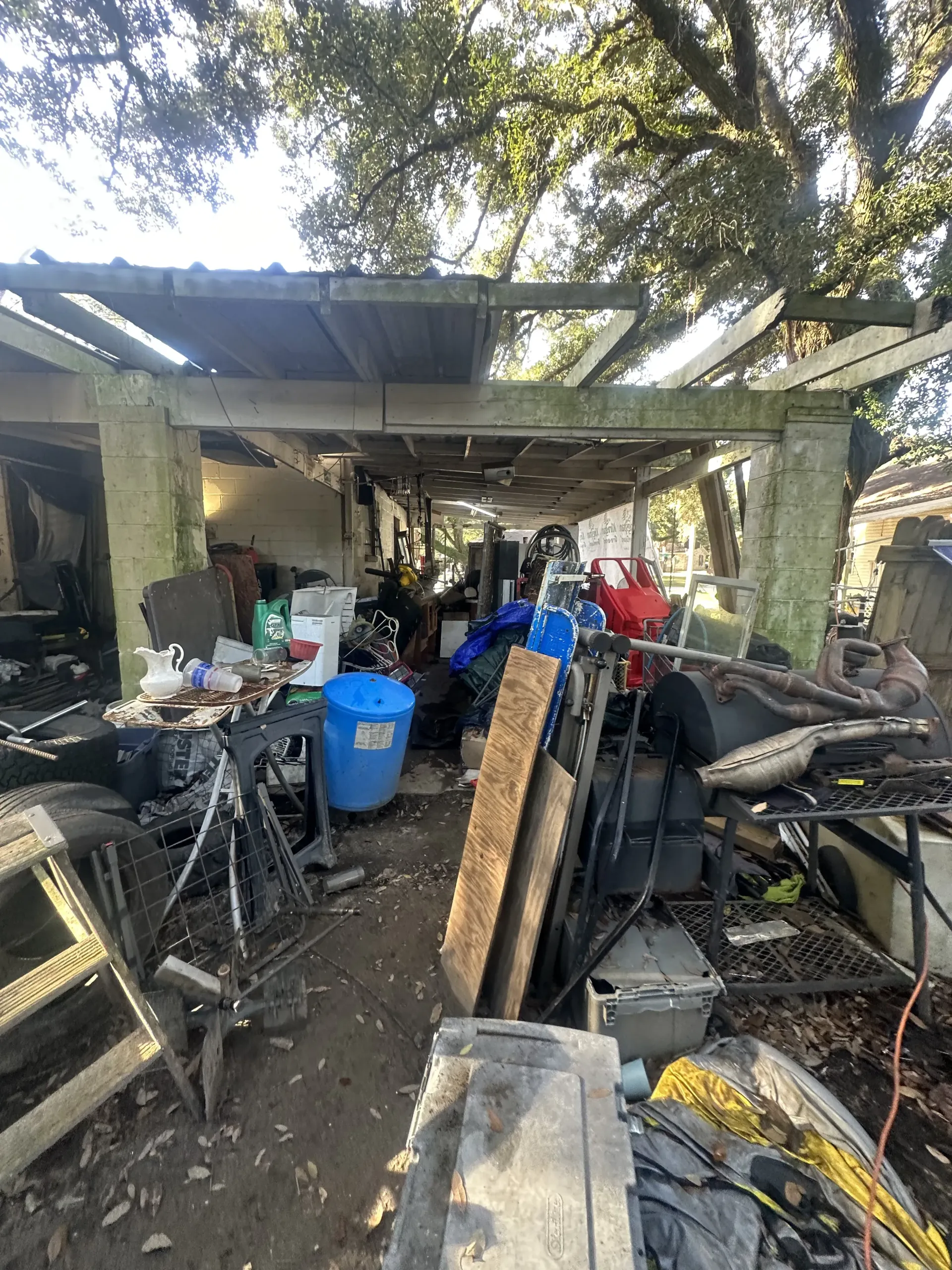 Cluttered outdoor shed with tools, bins, scrap wood, and metal under a corrugated roof.