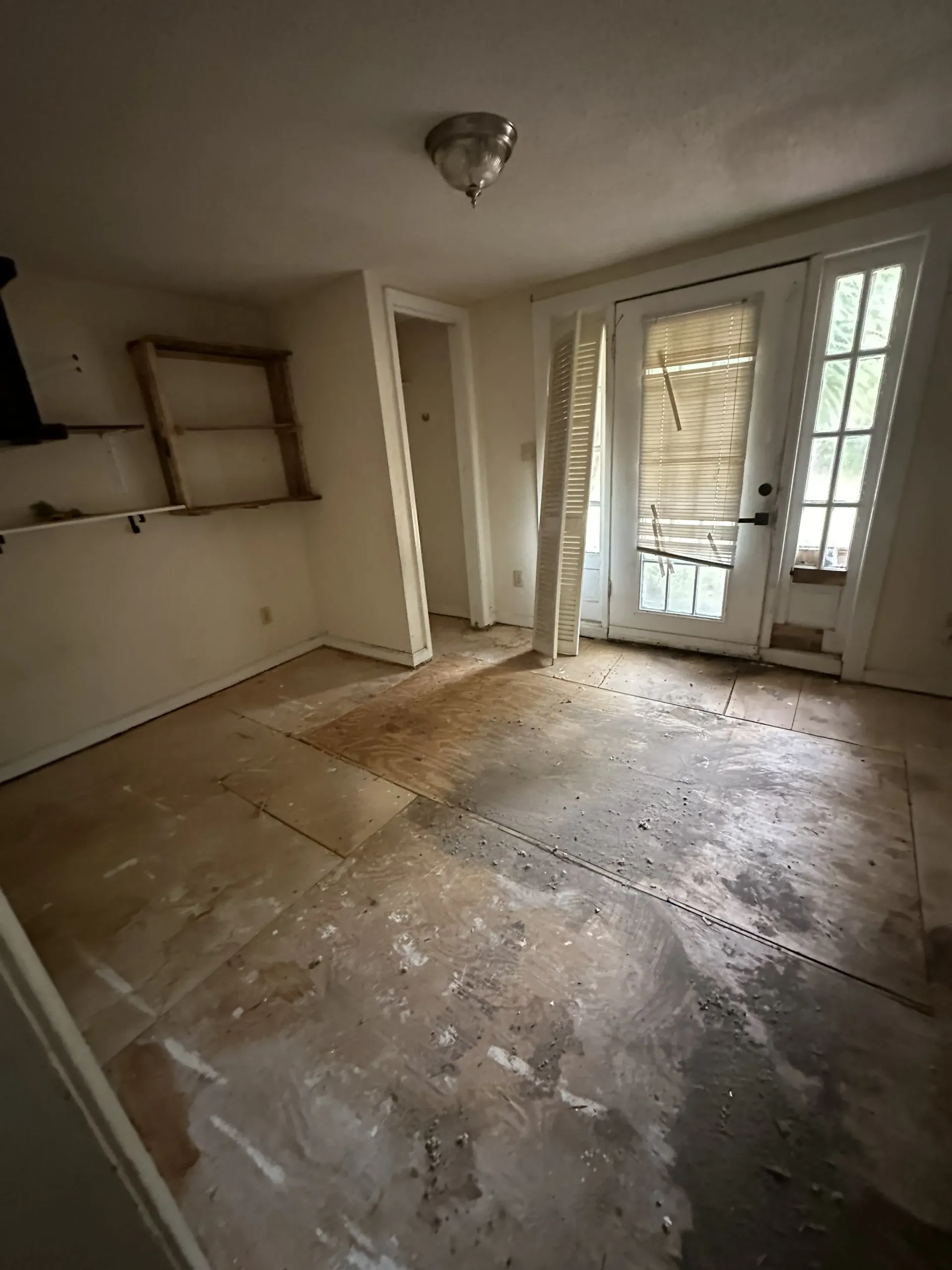 Empty, unfinished room with bare floors, white walls, and glass doors letting in daylight