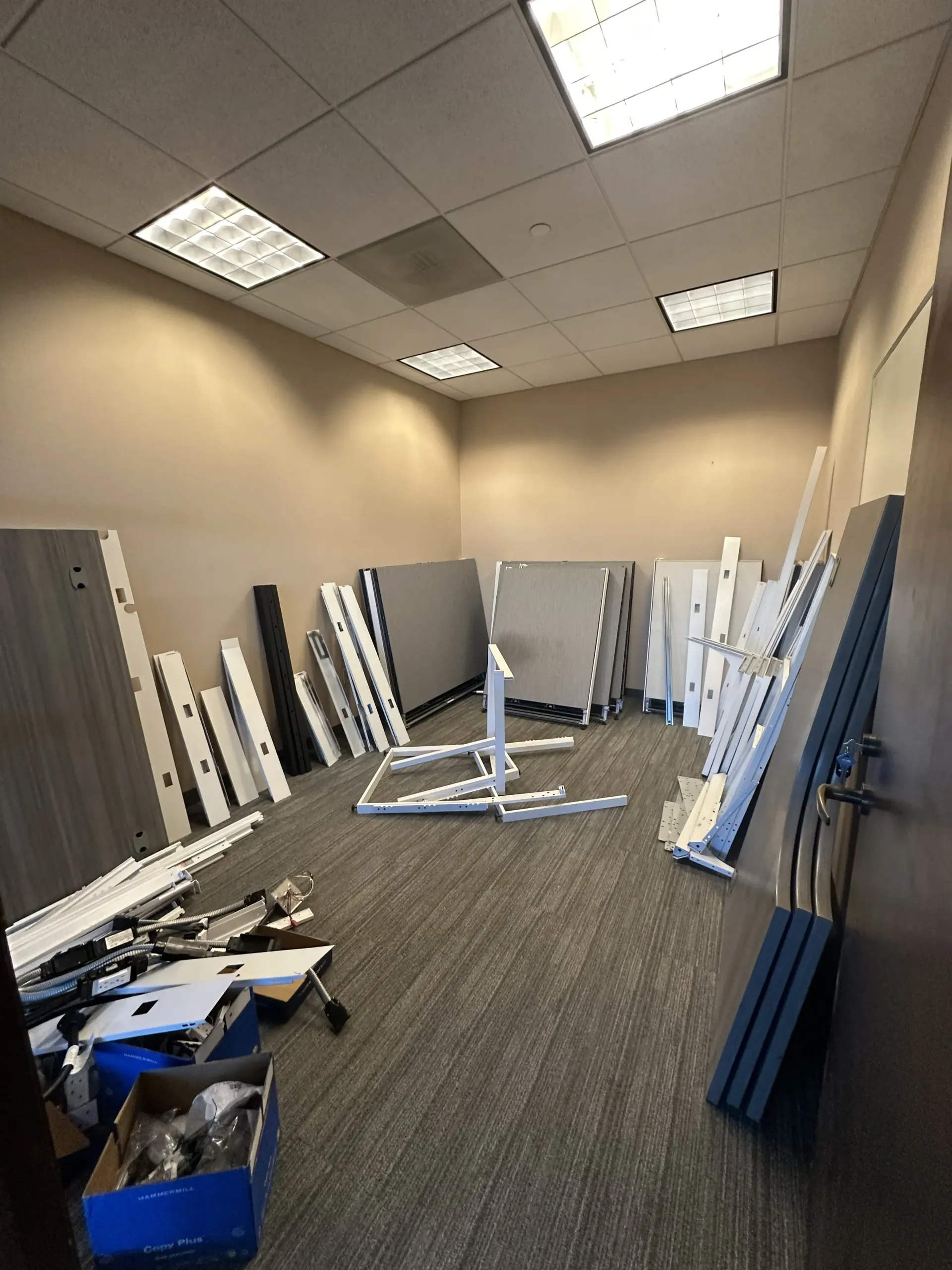 Empty office room with disassembled white and blue furniture parts leaning against the walls.