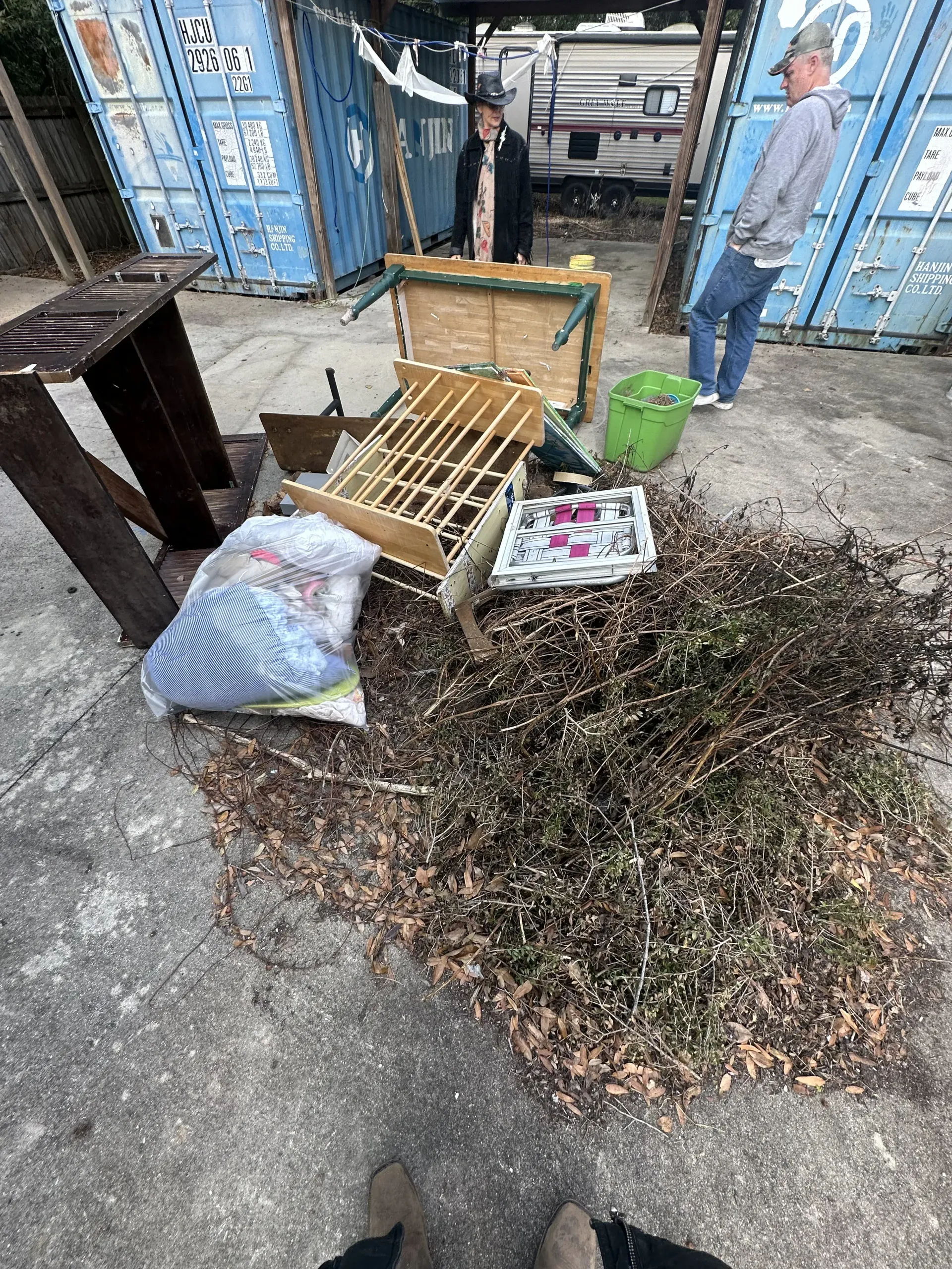 Pile of leaves and debris on a sidewalk outside a shop, with a broken chair, cushion, and buckets nearby.