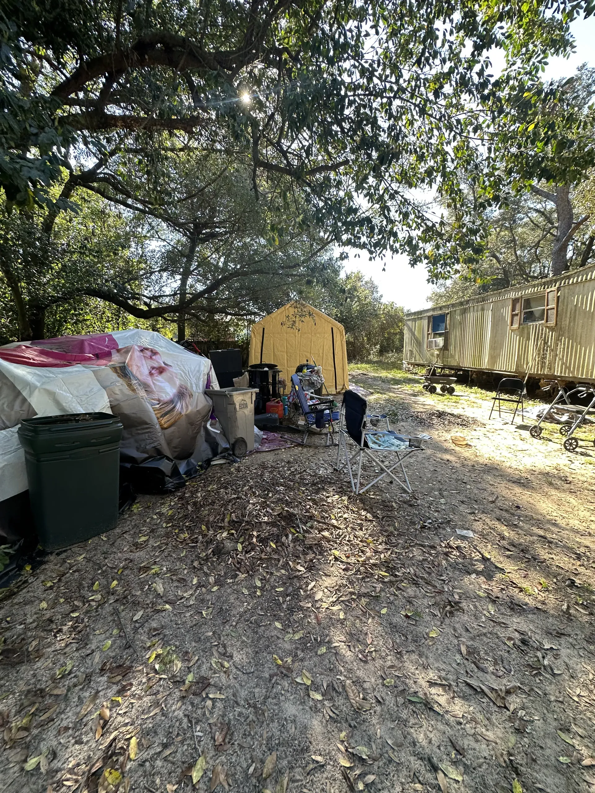 Trash bins and bags beside a yellow train car in a leafy outdoor area, with a person nearby