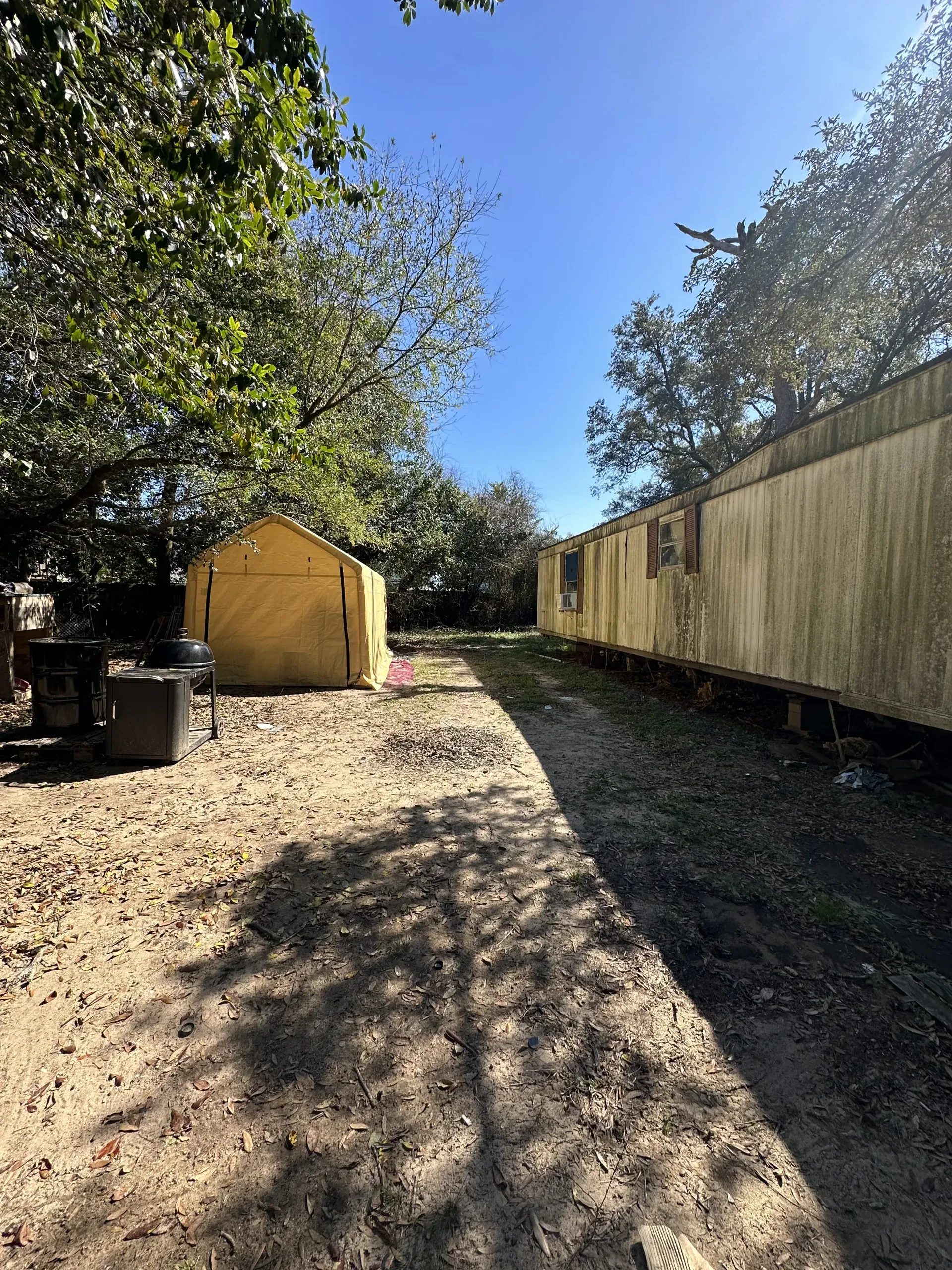 Backyard with a small yellow shed, long fence, and dappled sunlight on a dirt path