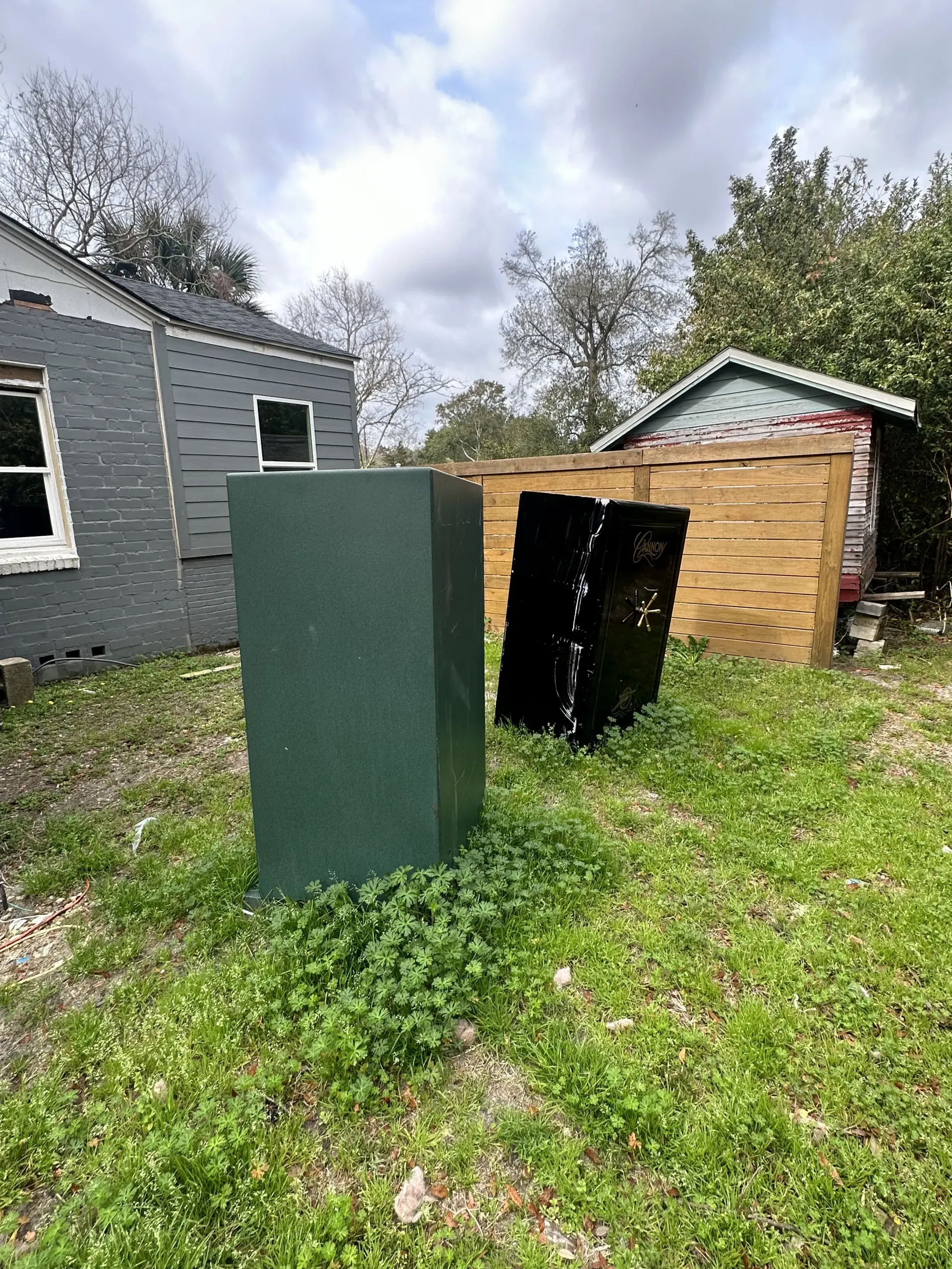 Green cabinet and black panels outdoors between two sheds on a grassy yard