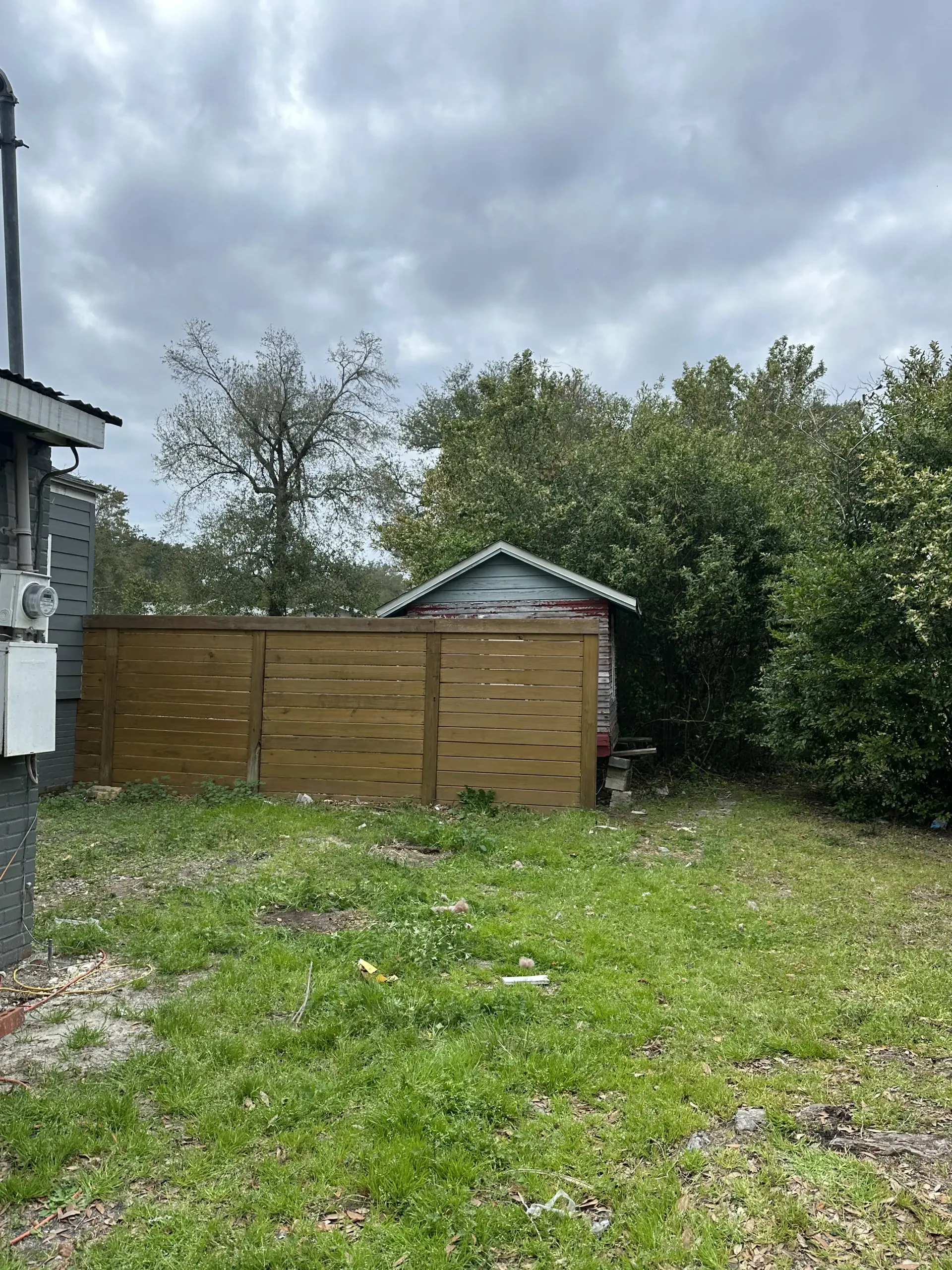 Grassy backyard with wooden fence, small shed, and cloudy sky