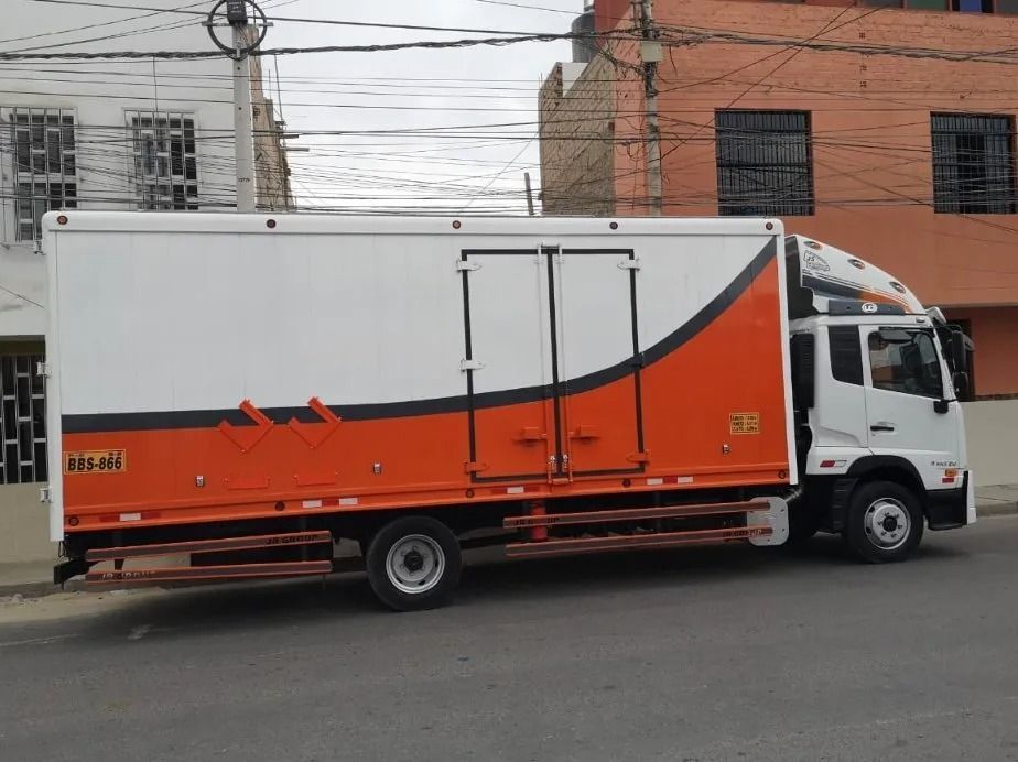 Camión de reparto blanco y naranja estacionado en una calle frente a edificios de apartamentos.