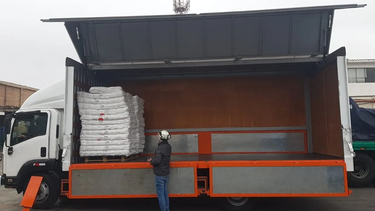 Trabajadores cargando palés envueltos en un camión de reparto blanco con un panel lateral abierto.