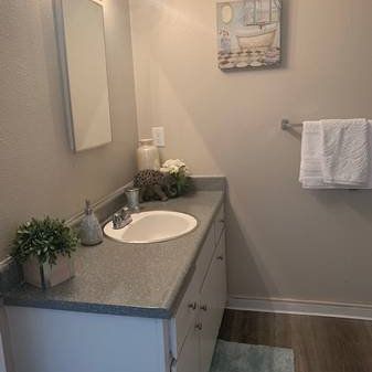 Small bathroom vanity with gray countertop, sink, mirror, towel rack, and wall art.