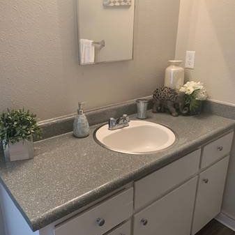 Small bathroom vanity with gray countertop, white sink, mirror, and decorative items near the faucet.