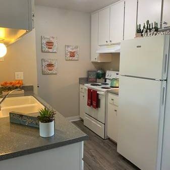 Bright white kitchen with gray island countertop, white cabinets, fridge, stove, and red towels