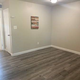 Empty gray room with wood-look flooring, white trim, and a small wall sign near a doorway