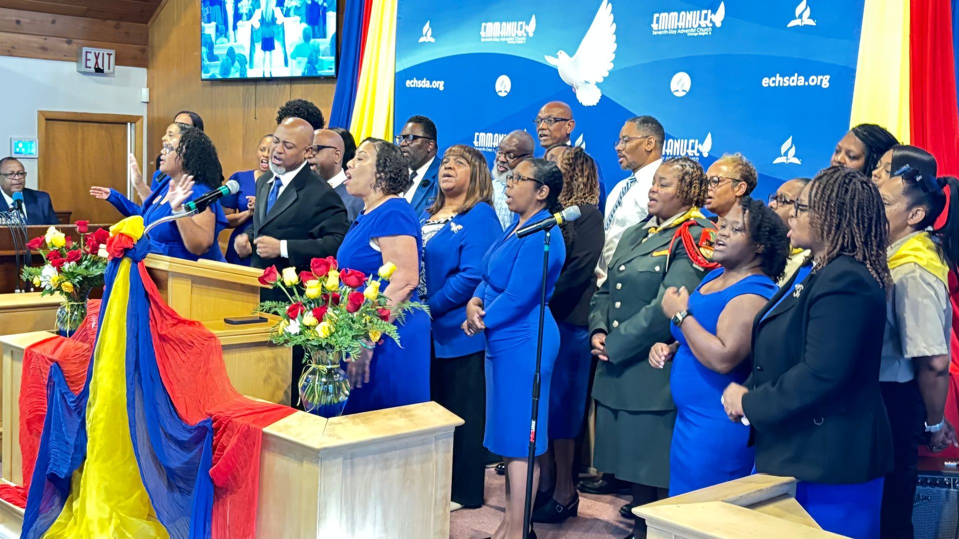 Group of people in blue attire standing on a stage beside a lectern with flowers and a colorful backdrop