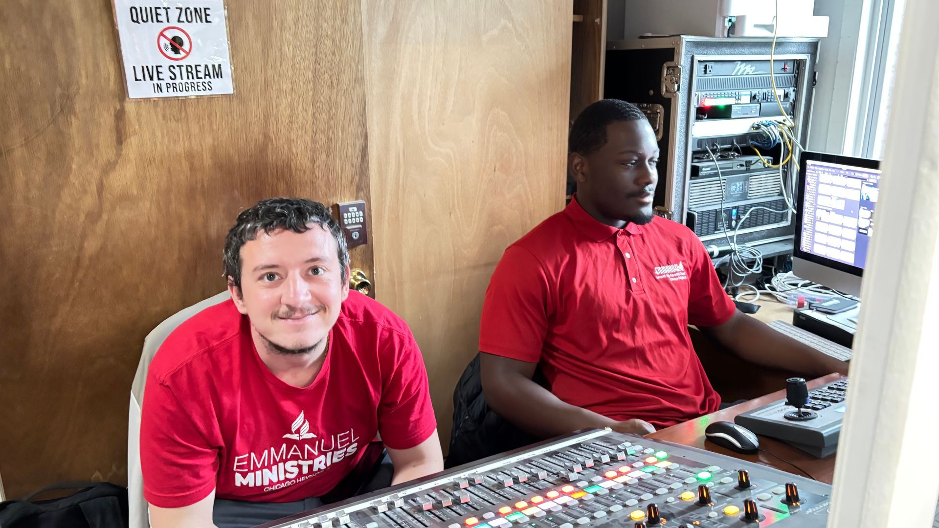 Two people in red shirts at a radio control panel, one smiling toward the camera.