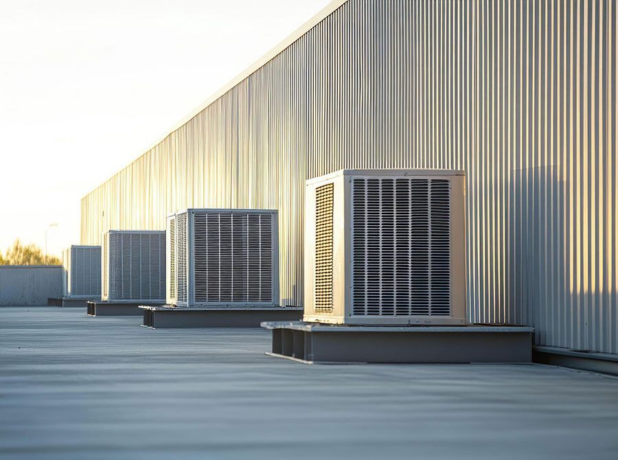 Rooftop HVAC units lined along a corrugated metal building in bright daylight
