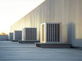 Rooftop row of large HVAC units beside a beige industrial building at sunset