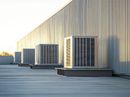 Rooftop row of large HVAC units beside a beige industrial building at sunset