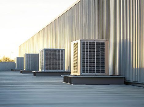 Rooftop row of large HVAC units beside a beige industrial building at sunset