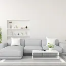 Minimalist white living room with a light gray sectional sofa, coffee table, and wall shelves with decor.
