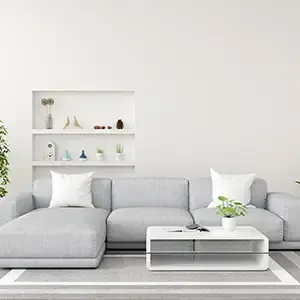 Minimalist white living room with a light gray sectional sofa, coffee table, and wall shelves with decor.