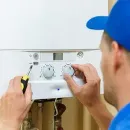 Technician adjusting a boiler control panel with a screwdriver and knob