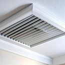 White ceiling air vent with adjustable slats in a corner near the molding