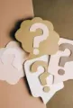 Paper question marks in white and tan on a brown background
