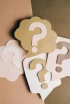 Paper question marks in white and tan on a brown background