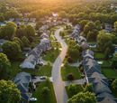 Aerial view of a suburban neighborhood at sunset with curving streets and rows of houses.