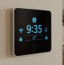 Wall-mounted smart thermostat showing 9:35, 21°, and Wi‑Fi, lock, and home icons on a black screen