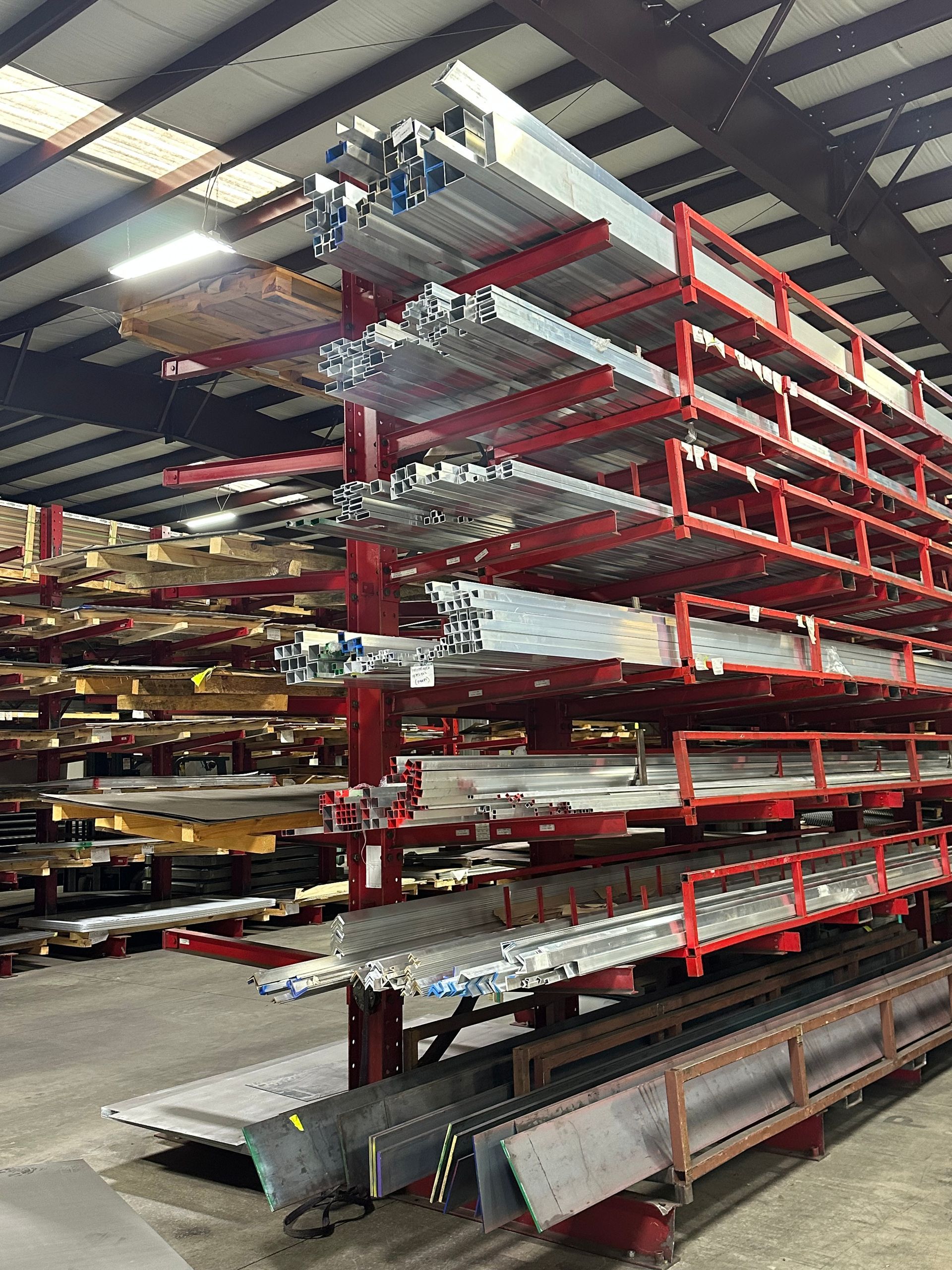 Metal angles and flat sheets stored on red industrial shelving.
