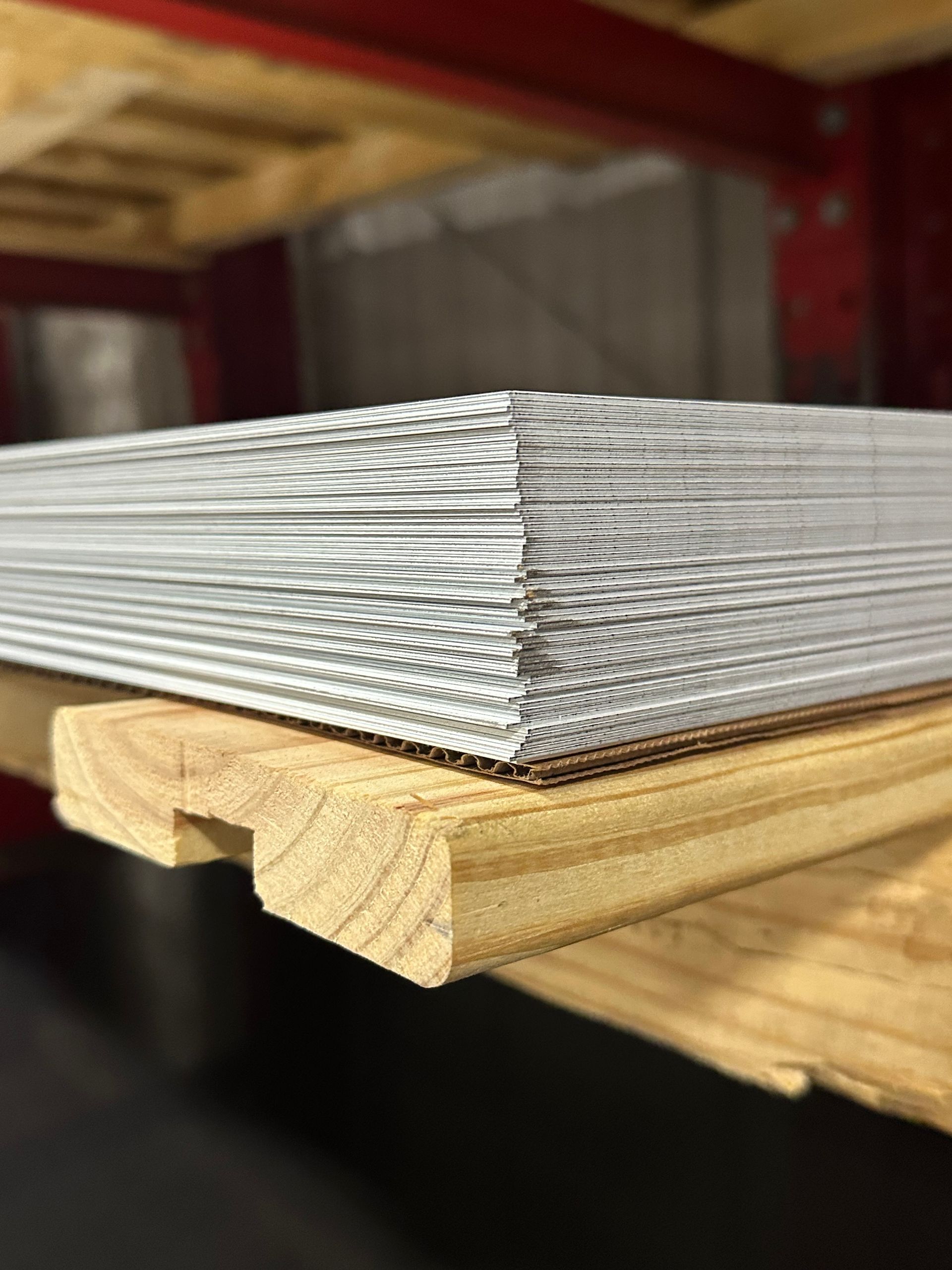Metal angles and flat sheets stored on red industrial shelving.