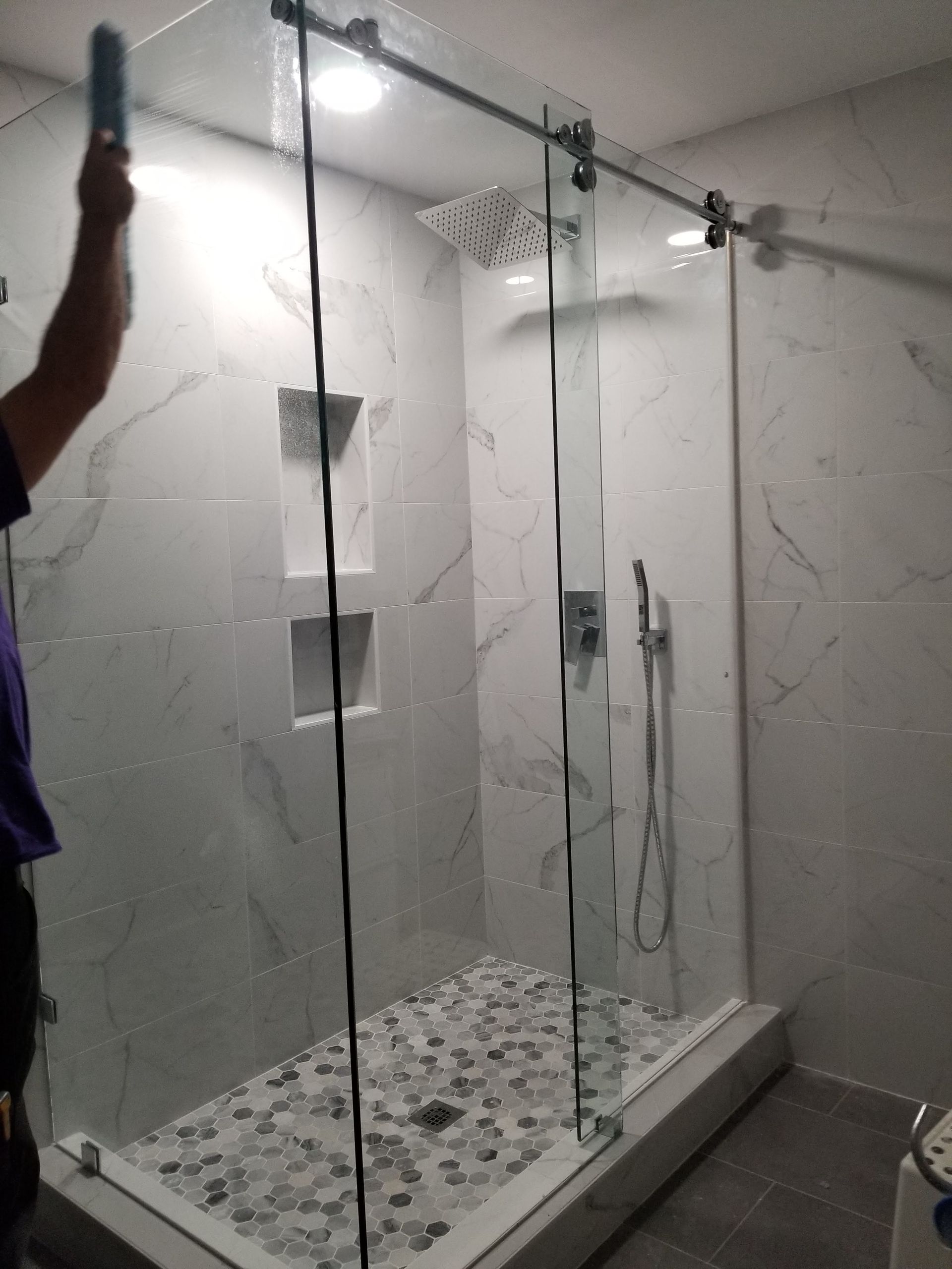 A man is cleaning a glass shower door in a bathroom.