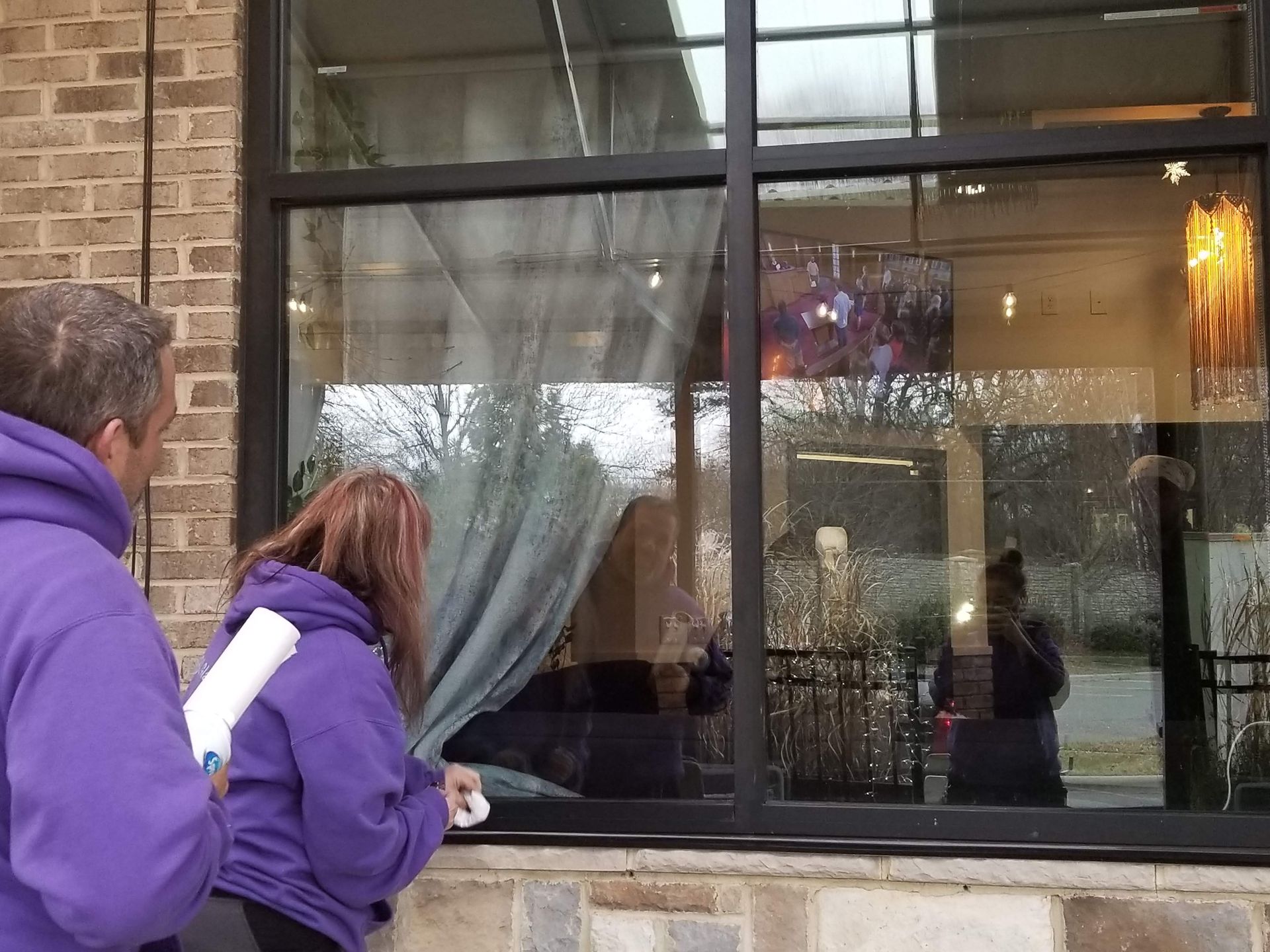 A man and a woman are cleaning a window outside of a building.