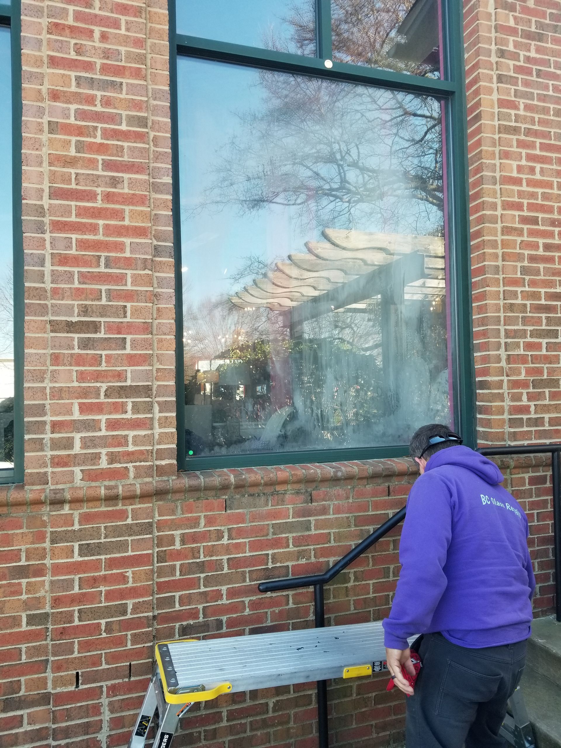 A man in a purple hoodie is cleaning a window on a brick building.