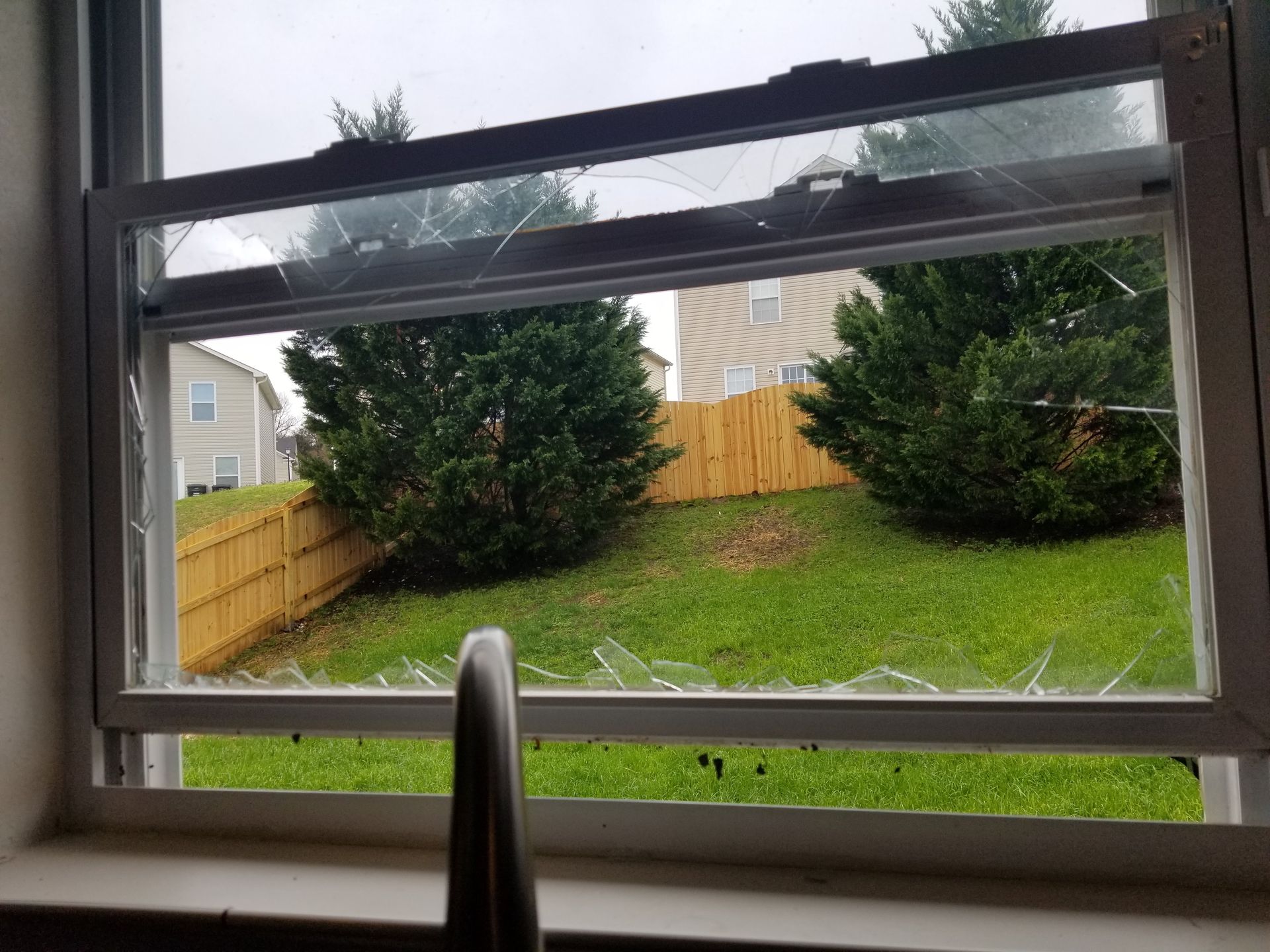 A broken window with a view of a yard and a fence.
