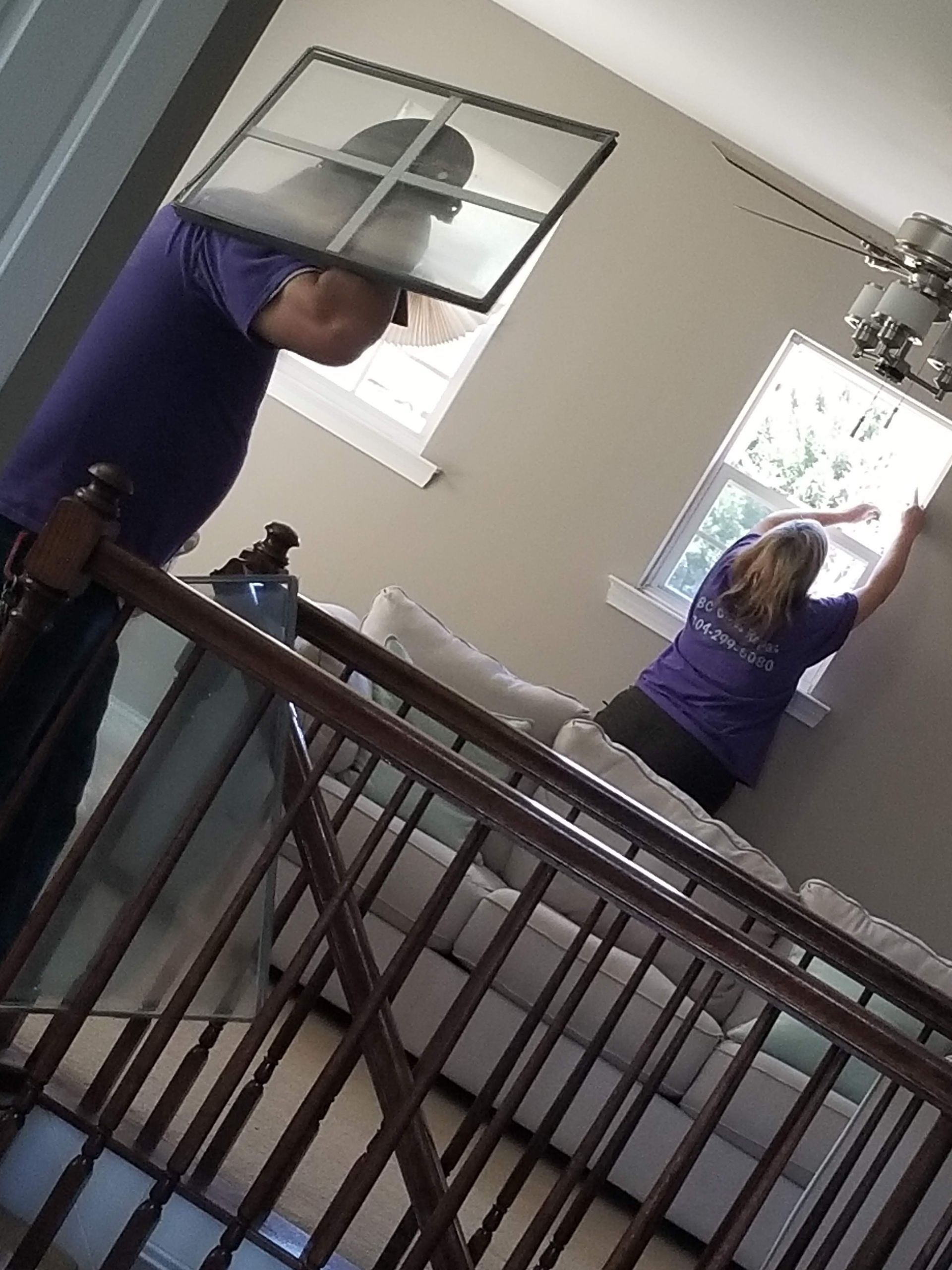A man and a woman are cleaning a window in a living room.
