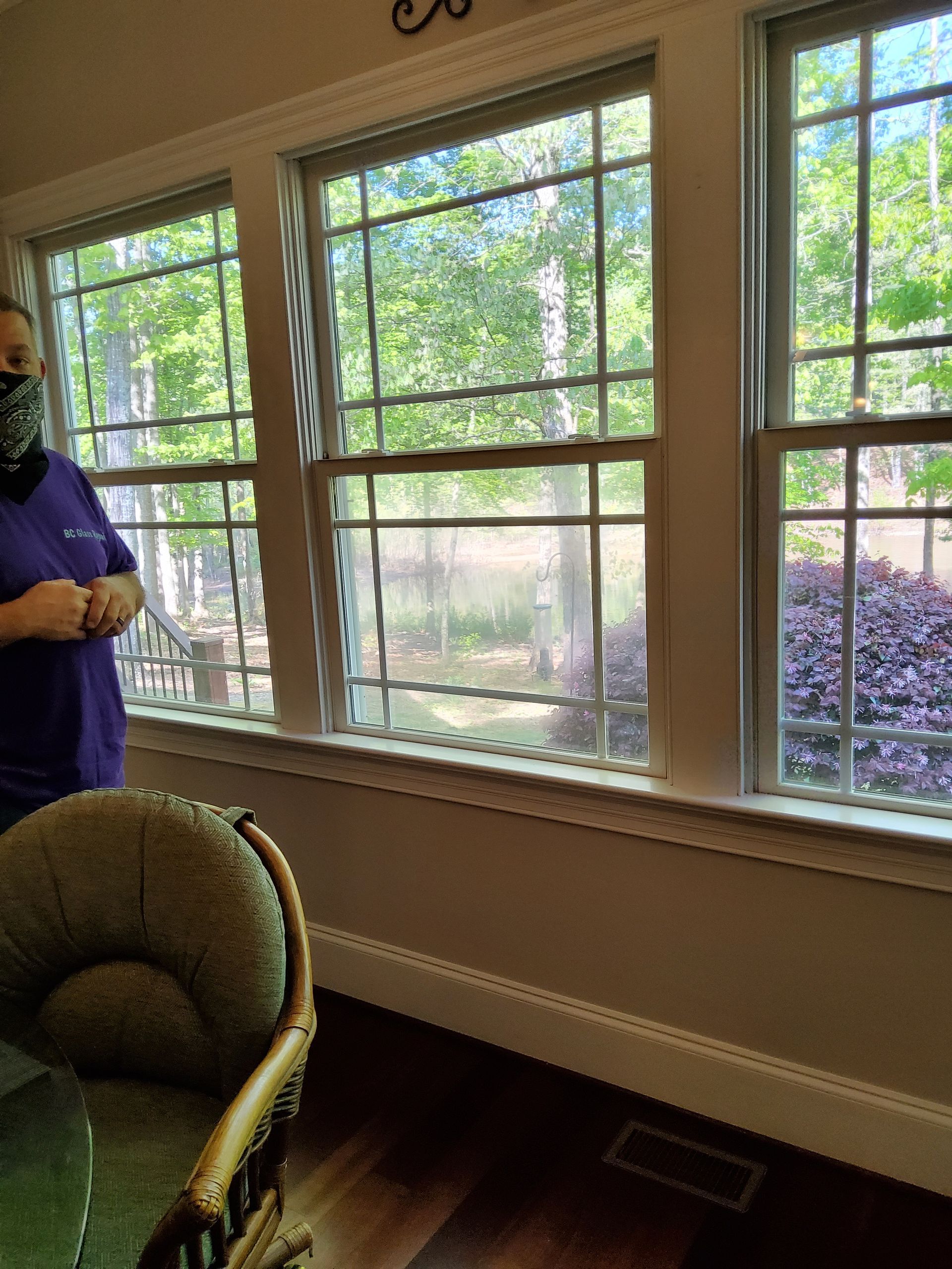 A man wearing a mask is standing in front of a window in a living room.